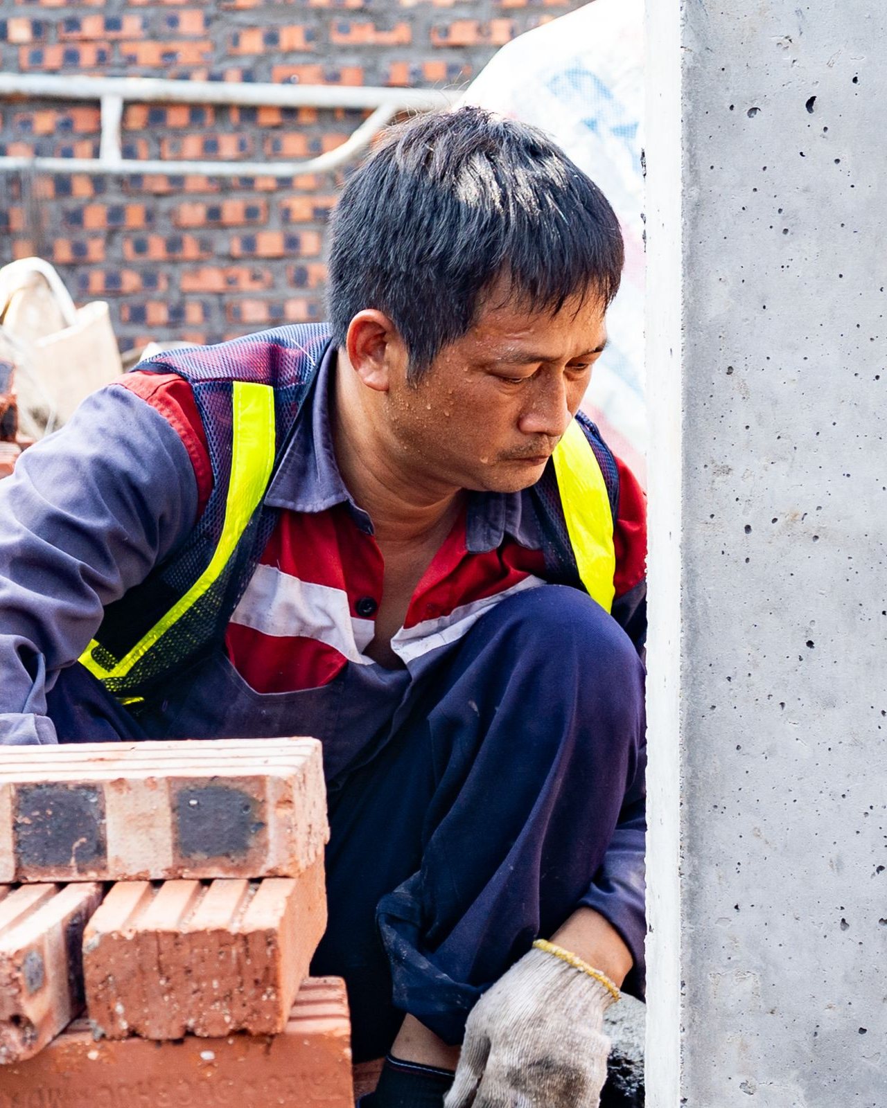 A construction worker in overalls and a hi-vis vest laying bricks on a Singapore building site.